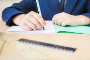 Desktop of student sitting at desk, with a ruler, writing and doing classwork