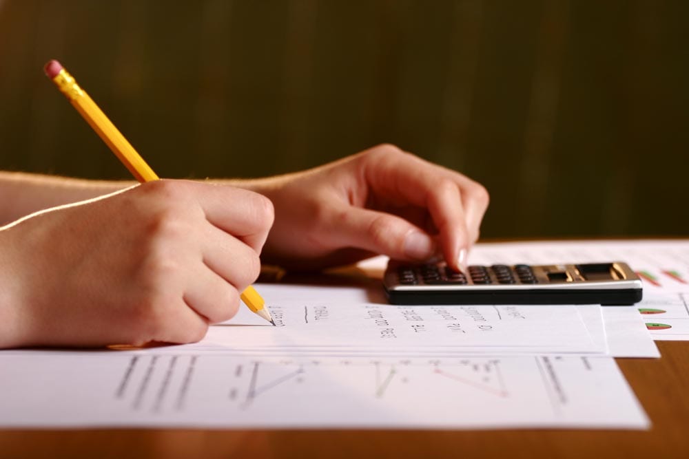 Close-up of hands with a pen and calculator on some document | Math Solutions