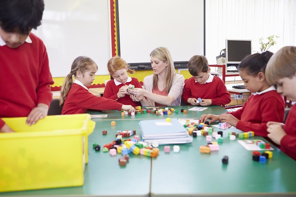 Primary School Pupils And Teacher Working With Coloured Blocks