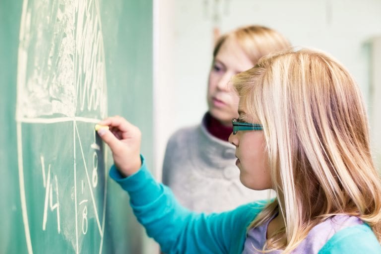 Preteen girl doing a fraction by drawing a pie on the chalk board under the supervision of her teacher. | Math Solutions, Classroom Lessons, Fun with Fractions