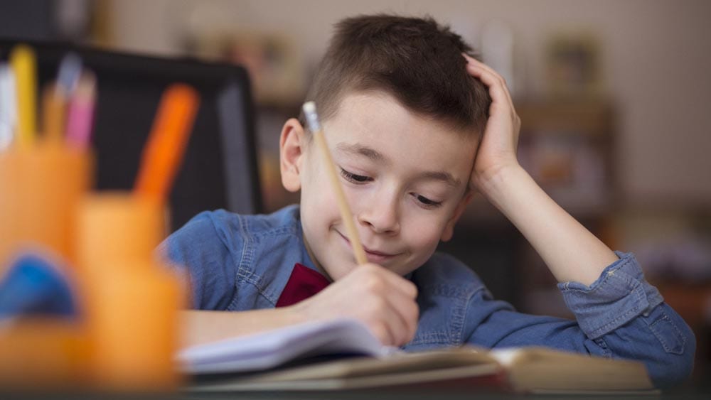 Portraits of cute little boy doing homework . Shallow DOF.