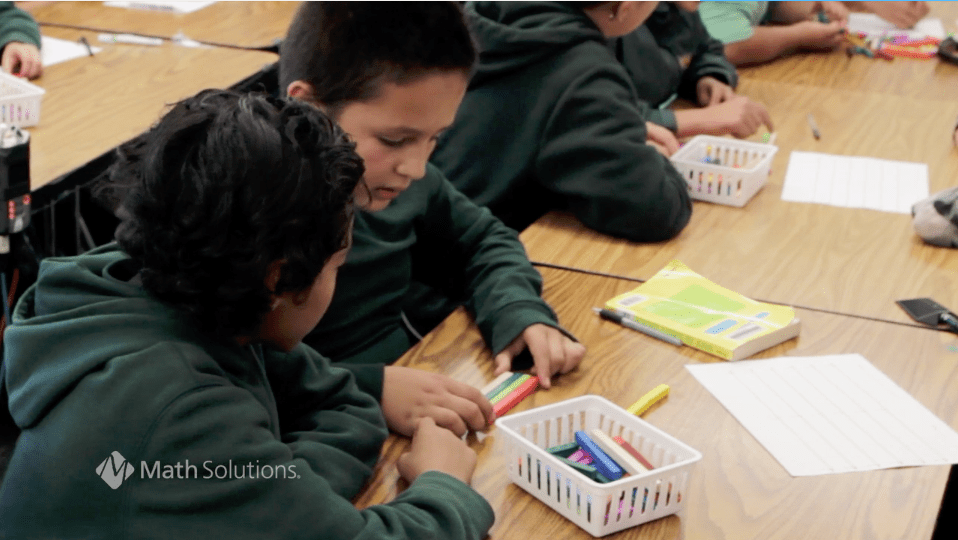 2 children in green school sweatshirts working with cuisenaire rods