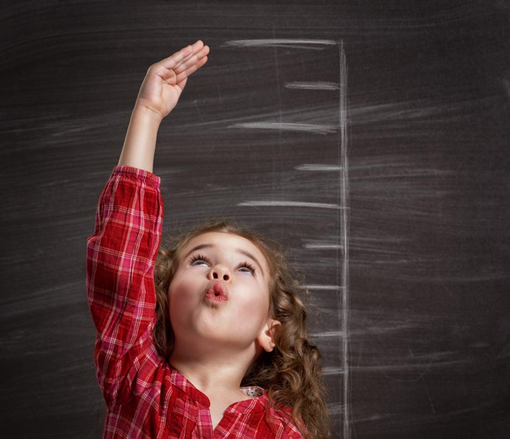 Young girl standing in front of a blackboard estimating her heigth